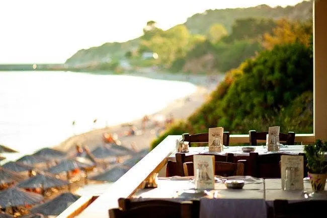 A taverna terrace overlooking a beach, with set tables in the foreground